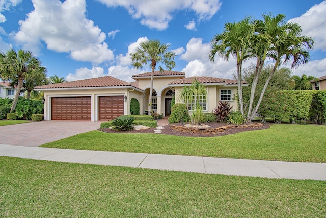 mediterranean / spanish-style home featuring decorative driveway, stucco siding, an attached garage, a tiled roof, and a front lawn