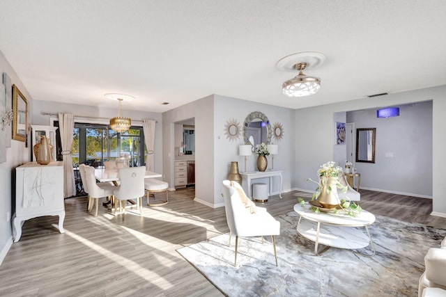 living area featuring a notable chandelier, wood finished floors, visible vents, and baseboards