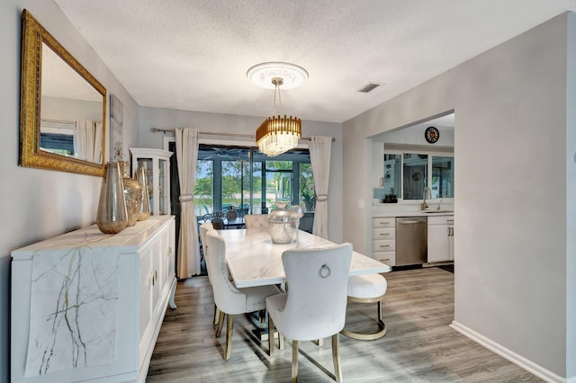 dining room with light wood-type flooring, baseboards, visible vents, and a textured ceiling