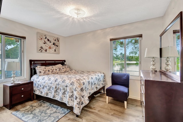 bedroom with a textured ceiling, baseboards, and light wood-style floors