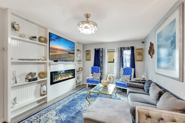 living room with wood finished floors, a glass covered fireplace, and built in shelves