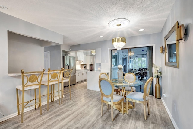 dining area with light wood-style floors, a chandelier, a textured ceiling, and baseboards