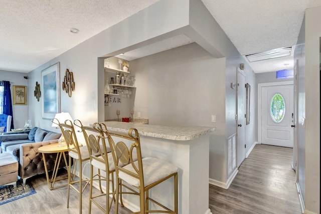 kitchen featuring a textured ceiling, light countertops, a kitchen bar, and wood finished floors