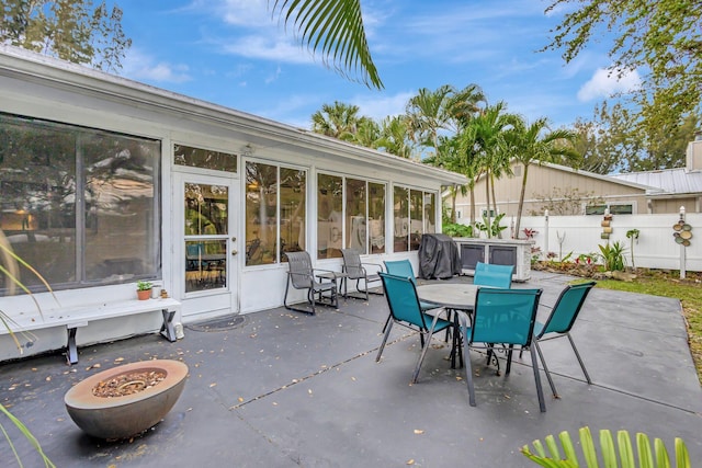 view of patio with outdoor dining space, fence, and a sunroom