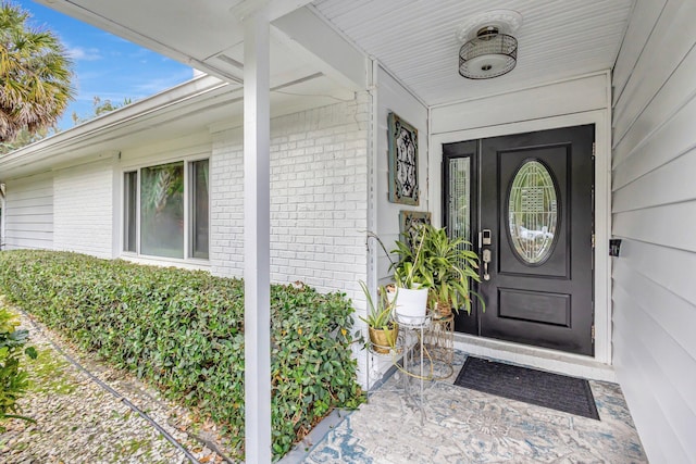 view of exterior entry featuring a porch and brick siding