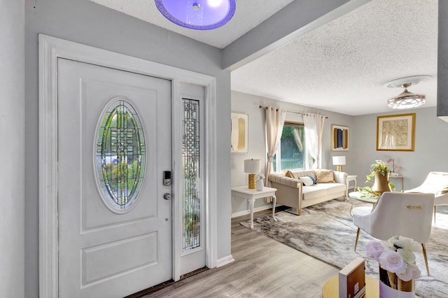 foyer entrance featuring a textured ceiling, baseboards, and light wood-style floors