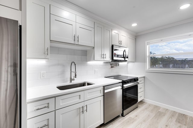 kitchen featuring light countertops, backsplash, appliances with stainless steel finishes, a sink, and baseboards