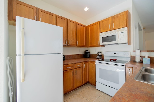 kitchen with light tile patterned floors, white appliances, brown cabinets, and a sink