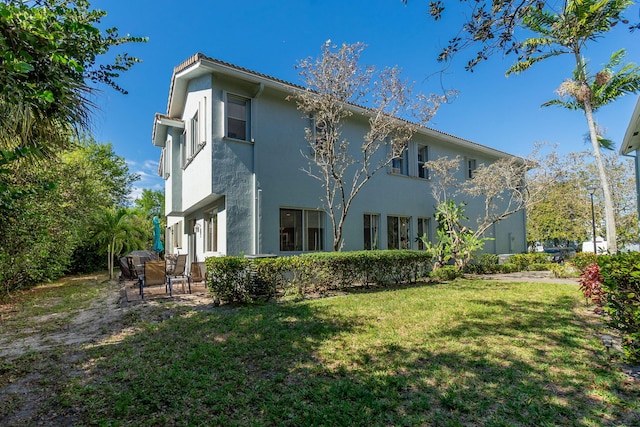 back of property featuring a patio area, a lawn, and stucco siding