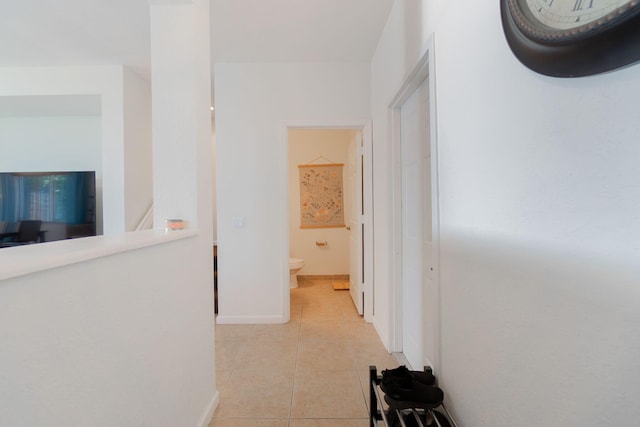 corridor with light tile patterned floors, an upstairs landing, and baseboards