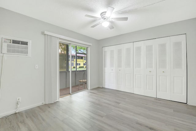 unfurnished bedroom featuring light wood finished floors, ceiling fan, access to exterior, a textured ceiling, and a wall mounted AC