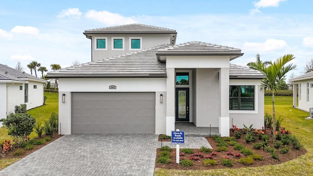 prairie-style house with an attached garage, a tiled roof, decorative driveway, stucco siding, and a front yard