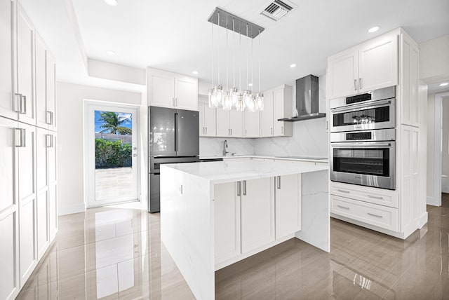 kitchen featuring visible vents, backsplash, a center island, stainless steel appliances, and wall chimney range hood