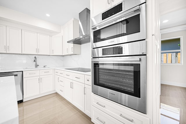 kitchen with a sink, backsplash, white cabinetry, wall chimney range hood, and dishwasher