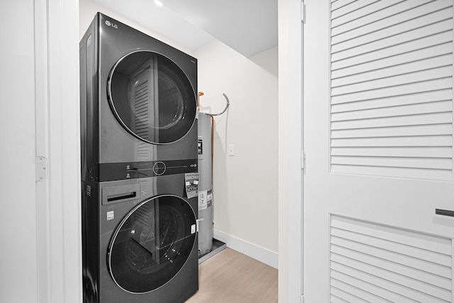 clothes washing area with baseboards, stacked washer and clothes dryer, wood finished floors, and laundry area