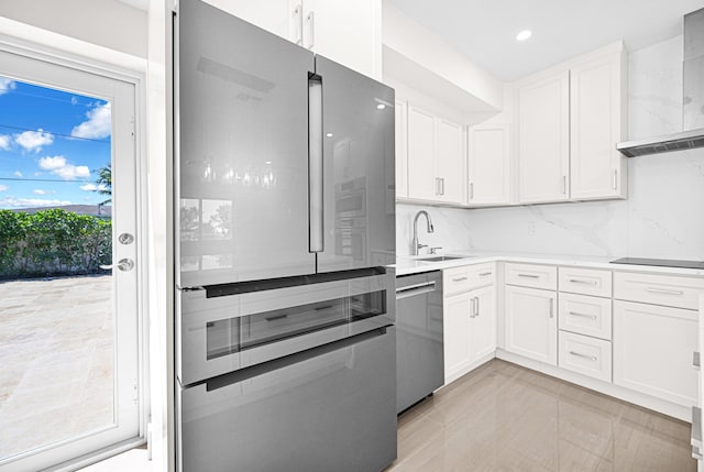 kitchen featuring a sink, stainless steel appliances, light countertops, white cabinetry, and wall chimney range hood