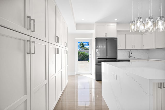 kitchen with light stone countertops, freestanding refrigerator, a sink, white cabinets, and tasteful backsplash