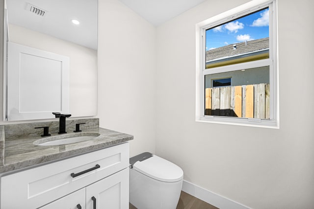 bathroom featuring visible vents, baseboards, toilet, wood finished floors, and vanity