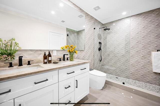 bathroom with a sink, toilet, double vanity, and a walk in shower