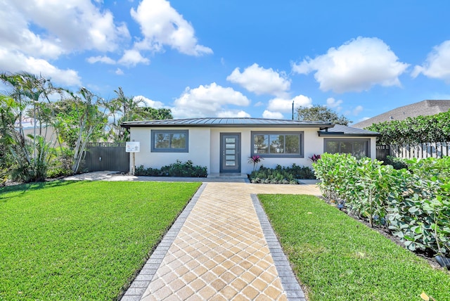 single story home featuring stucco siding, a front lawn, a standing seam roof, fence, and metal roof