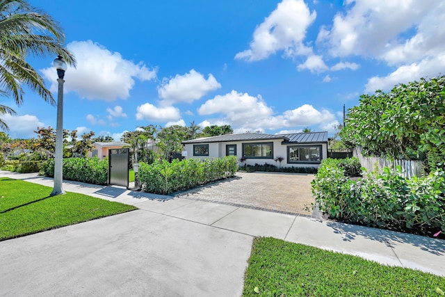 view of front of property with a front yard, fence, a standing seam roof, stucco siding, and metal roof