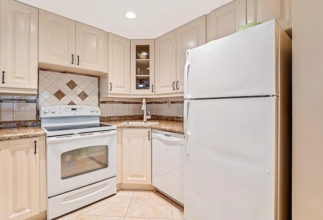 kitchen featuring backsplash, glass insert cabinets, light tile patterned flooring, a sink, and white appliances