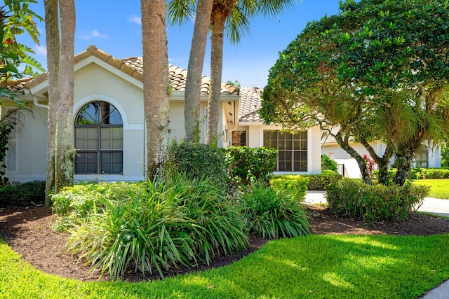 view of front of property featuring a tiled roof, a front lawn, and stucco siding