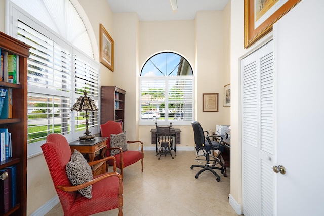 home office with a high ceiling, light tile patterned flooring, and baseboards