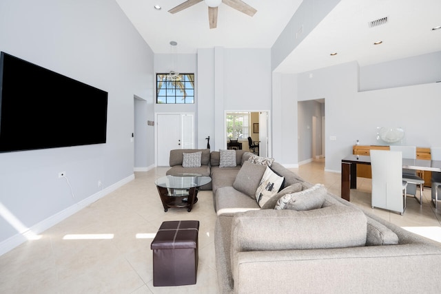 living area with light tile patterned floors, visible vents, a high ceiling, ceiling fan, and baseboards