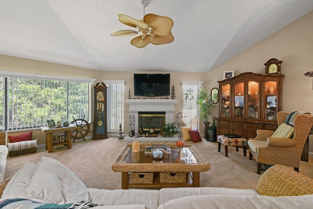 living area featuring carpet floors, vaulted ceiling, a glass covered fireplace, a textured ceiling, and a ceiling fan