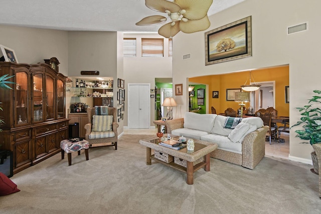 carpeted living area with visible vents, baseboards, a high ceiling, and ceiling fan