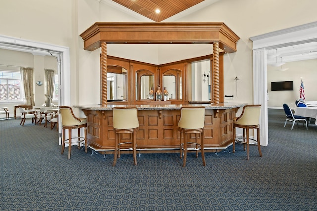 bar with high vaulted ceiling, dark carpet, a bar, and baseboards