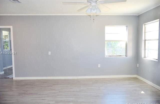 spare room featuring wood finished floors, visible vents, a ceiling fan, baseboards, and ornamental molding