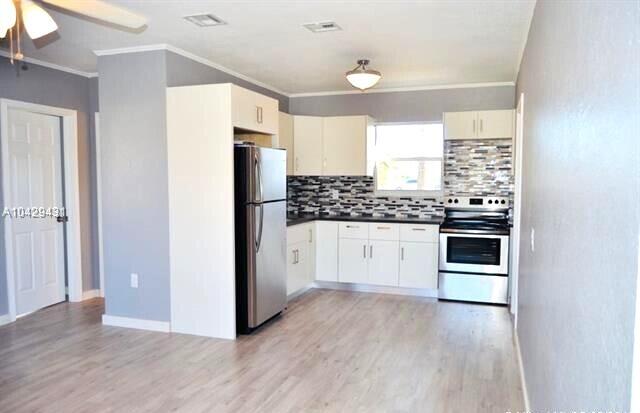 kitchen featuring dark countertops, decorative backsplash, light wood-style flooring, and appliances with stainless steel finishes