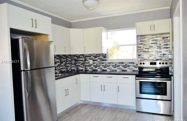 kitchen with decorative backsplash, dark countertops, appliances with stainless steel finishes, ornamental molding, and light wood-type flooring