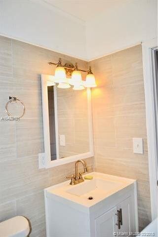 bathroom with toilet, tile walls, and vanity