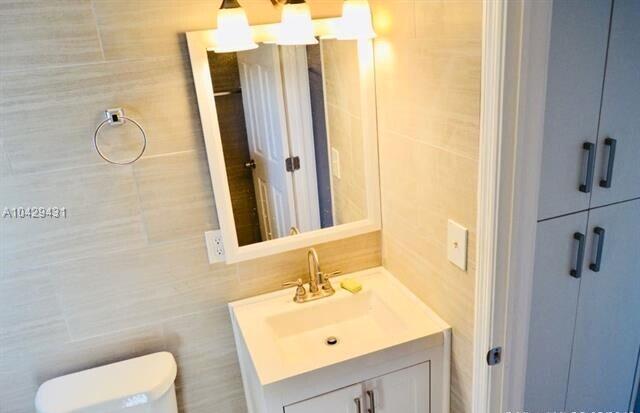 half bathroom featuring toilet, tile walls, and vanity