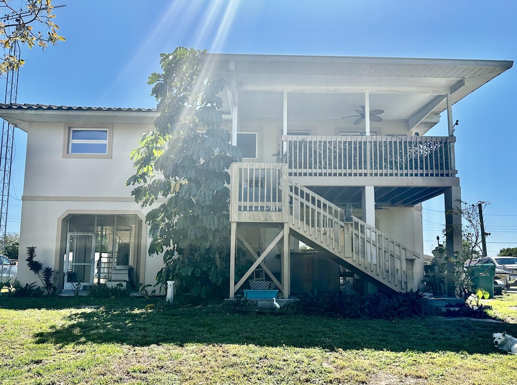 back of house with stucco siding, a ceiling fan, stairs, and a yard