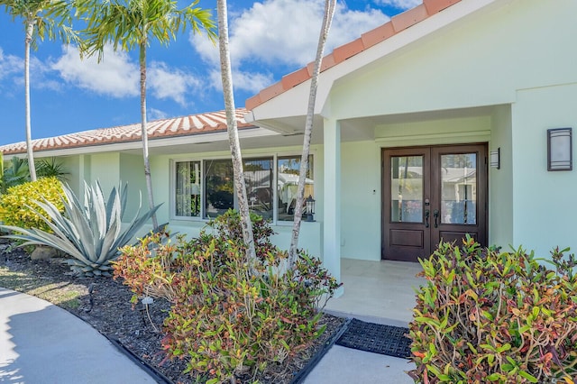 property entrance with a tiled roof, stucco siding, and french doors