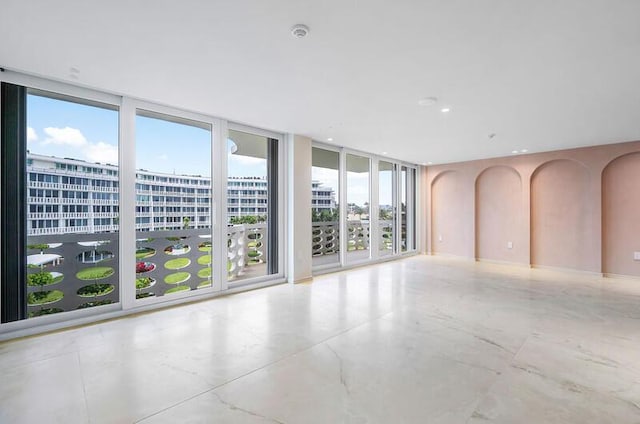 spare room featuring arched walkways, a city view, baseboards, marble finish floor, and expansive windows