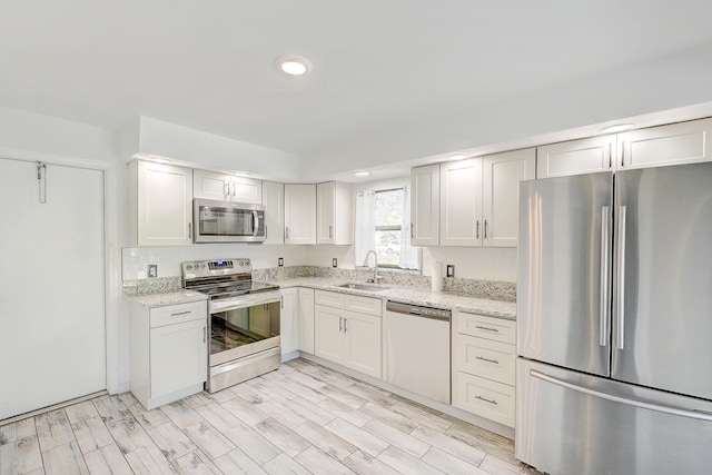 kitchen with wood finish floors, a sink, recessed lighting, appliances with stainless steel finishes, and light stone countertops