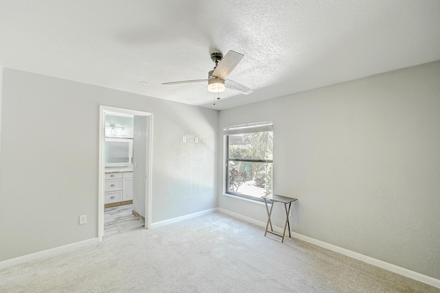 unfurnished room with a textured ceiling, a ceiling fan, baseboards, and light carpet