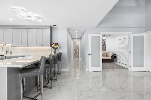 kitchen with marble finish floor, a breakfast bar area, light countertops, a sink, and baseboards