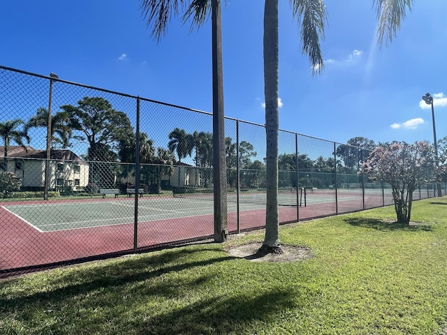 view of tennis court with a yard and fence