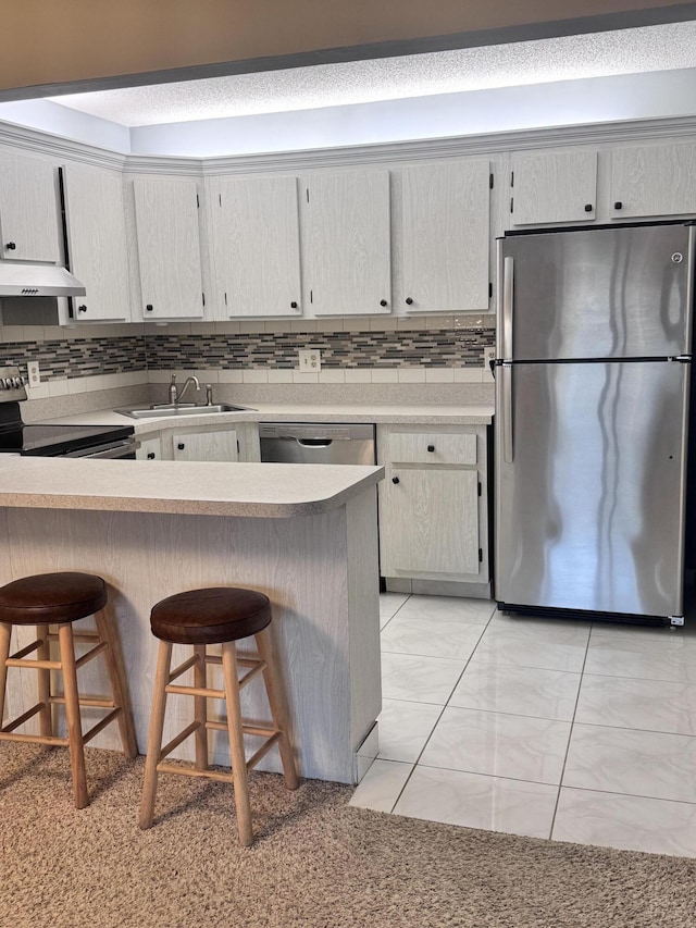 kitchen with stainless steel appliances, decorative backsplash, light countertops, a kitchen breakfast bar, and exhaust hood