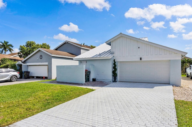 ranch-style home with decorative driveway, an attached garage, a standing seam roof, metal roof, and a front lawn