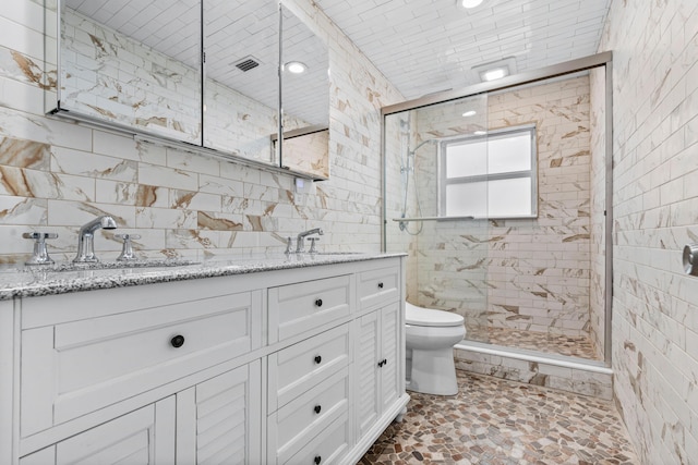 full bathroom with double vanity, a stall shower, tile walls, toilet, and a sink