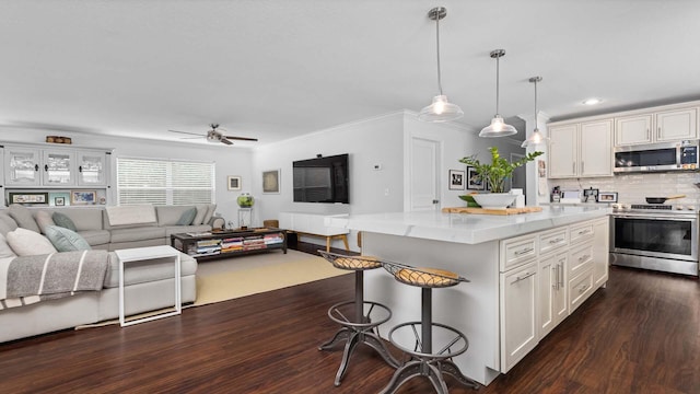 kitchen with stainless steel appliances, dark wood-type flooring, open floor plan, white cabinetry, and a kitchen bar