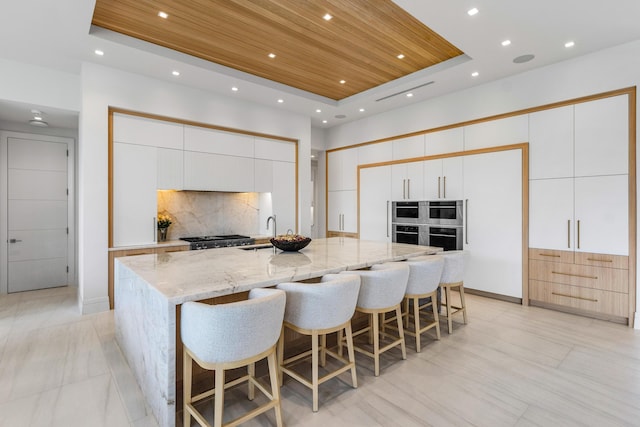 kitchen featuring a raised ceiling, decorative backsplash, wooden ceiling, modern cabinets, and a sink