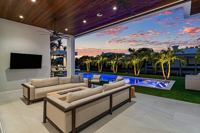 patio terrace at dusk featuring ceiling fan, a lawn, an outdoor living space with a fire pit, and an outdoor pool